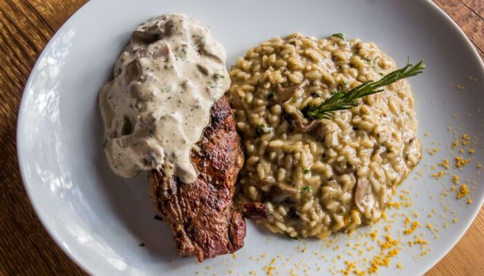 Delicious steak topped with sauce served with creamy mushroom risotto. Italian cuisine on a white plate. - Photo by Vinícius Caricatte on Pexels